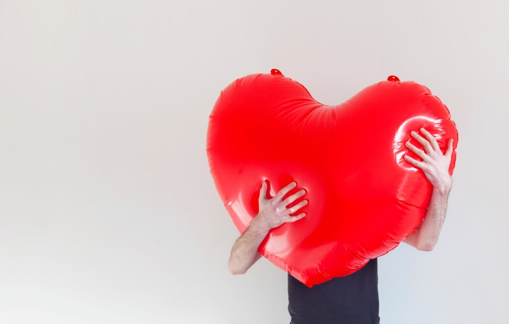 A person hugs a large red inflatable love heart. Health and love concept